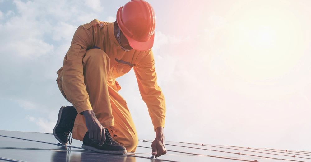 Arbeiter kniet auf einem Dach und installiert Sonnenkollektoren an einem sonnigen Tag