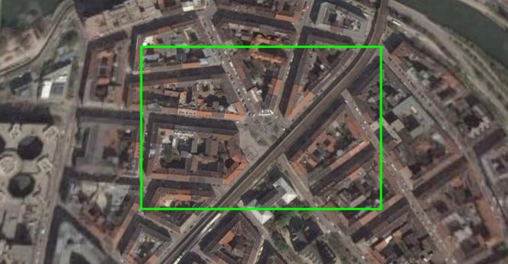 Satellitenbild zeigt urbane Gegend mit dicht gedrängten Gebäuden; einige Gebäude sind mit grünem Rechteck markiert; schmale Straßen trennen die Häuserblocks; ein Fluss verläuft am oberen Rand.