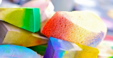 Bunte Schwämme liegen übereinander nah beieinander auf einem unscharfen Hintergrund.