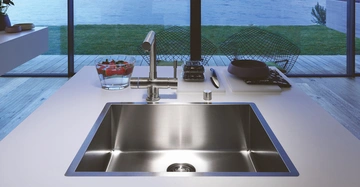 Ein Edelstahlspülbecken mit Wasserhahn in einer modernen Küche bereitet Essen vor Blick auf den Garten und den See durch große Fenster im Hintergrund