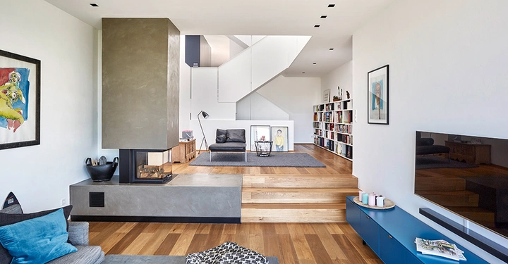 Galerie-Bild 4: Großer moderner Wohnraum zeigt Kamin in der Mitte hält den Raum warm hat bequeme Sitzgelegenheiten Bücherregal an der rechten Wand Treppe führt zum oberen Bereich.