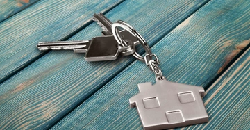 Schlüsselbund mit Hausanhänger liegt auf türkisfarbenem Holztisch