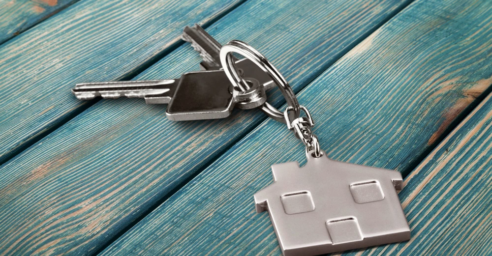 Schlüsselbund mit Hausanhänger liegt auf türkisfarbenem Holztisch