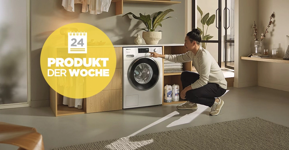 Person bedient Waschmaschine in modernem Hauswirtschaftsraum mit Holzregalen, Pflanzen und Reinigungsmitteln. Text im Bild: 24 PRODUKT DER WOCHE.