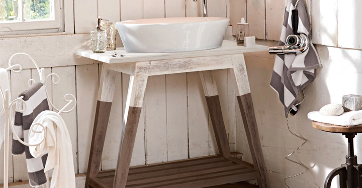 Galerie-Bild 12: Waschbecken stehend auf einem rustikalen Holzwaschtisch in einem weiß gestrichenen, holzgetäfelten Badezimmer mit Handtüchern und Accessoires umgeben von Fenstern und Tageslicht.