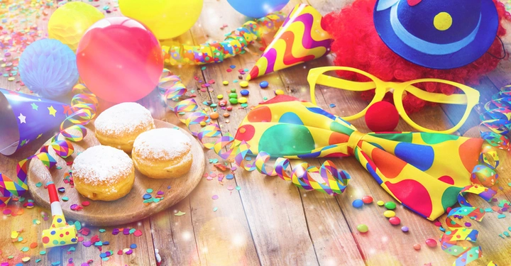 reich verzierter Holztisch mit Girlanden, Konfetti, Luftschlangen und 3 Faschingskrapfen auf einem bunten Pappteller. 