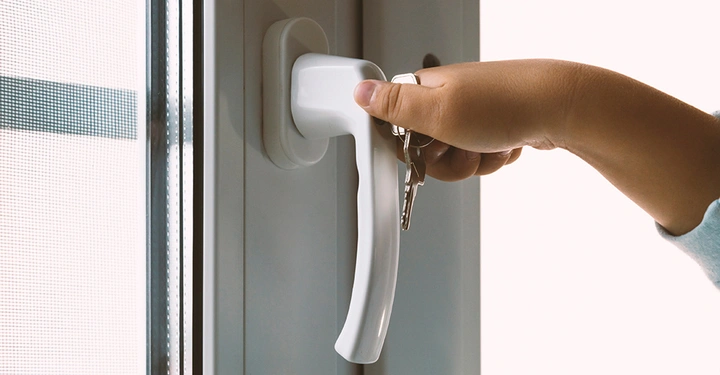 Hand hält Schlüssel und entriegelt weißen Fenstergriff in einem modernen Innenraum mit hellen Wänden