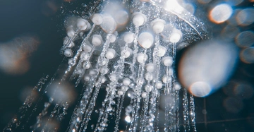 Duschkopf sprüht Wasserstrahlen in einer dunklen Umgebung mit verschwommenen Lichtflecken