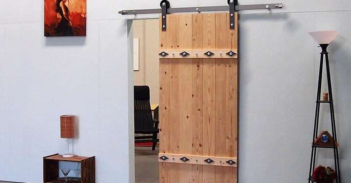 Holztür an einer Schiene gleitet in einem modernen Raum mit hellem Boden. Links ein Bild einer Frau. Lampe steht auf einem Regal und daneben ein Stuhl.