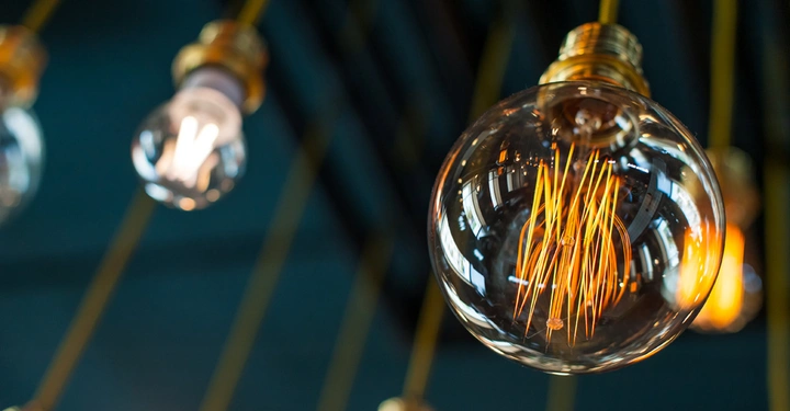 Mehrere Glühbirnen leuchten an gelben Kabeln von der Decke hängend, in einem dunklen Raum mit unscharfem Hintergrund.