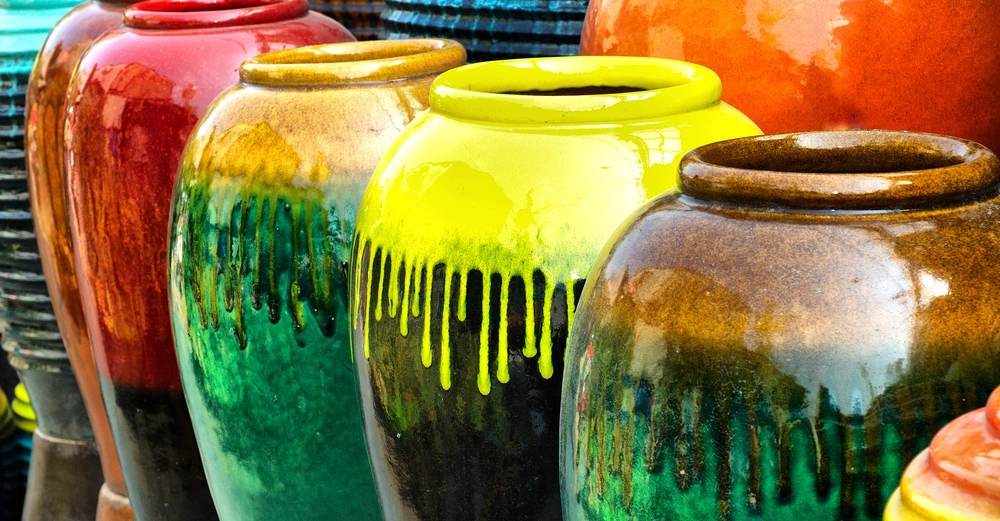 Bunte Keramiktöpfe in verschiedenen Glanzfarben stehen nebeneinander aufgereiht im Freien auf einem Markt oder Ausstellungsbereich