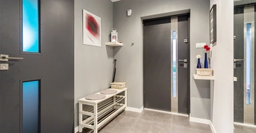 Flur mit grauer Wand und Boden Flur enthält schwarze Türen weiße Bank mit Kissen Wandregal mit Körben und Vasen minimalistische Dekoration und moderner Stil.