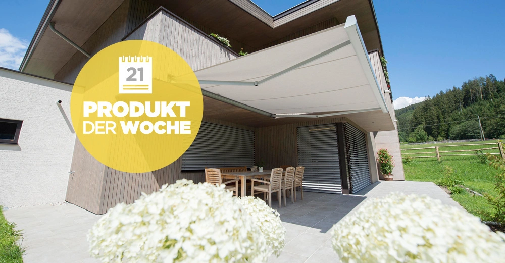 Eine Hausveranda mit Holztisch und Stühlen unter einer ausgefahrenen Markise in ländlicher Umgebung Text Produkt der Woche 21 in einem gelben Kreis