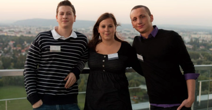 Galerie-Bild 40: Drei Personen stehen auf einem Balkon mit einer weitläufigen Stadtlandschaft im Hintergrund. Eine Person trägt einen gestreiften Pullover eine trägt eine schwarze Bluse und eine trägt einen schwarzen Pullover.