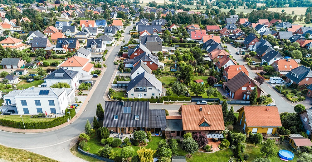 Drohnenaufnahme von Häusern in einer Vorstadt Die Häuser sind unterschiedlich gestaltet mit bunten Dächern und gepflegten Gärten Die Straßen sind gut geplant und Begrünung ist reichlich vorhanden