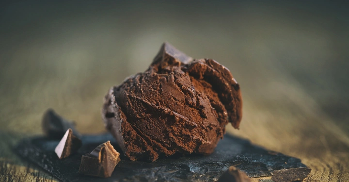 Eine Kugel Schokoladeneis mit Schokoladenstückchen liegt auf einem Schieferbrett in einem unscharfen hölzernen Hintergrund.