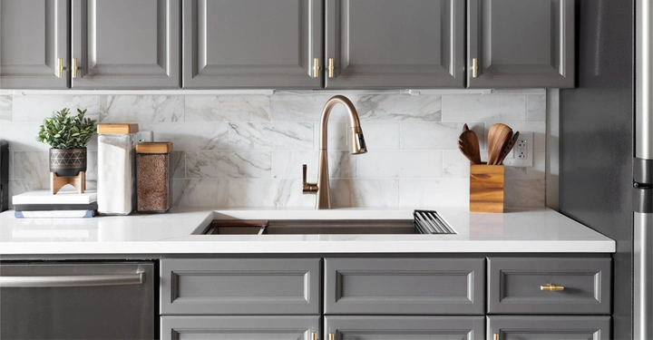 Landhausküche in grau, Arbeitsplatte und Küchenrückwand in weiß. Die Waschbeckenarmatur in warmem Messing. 