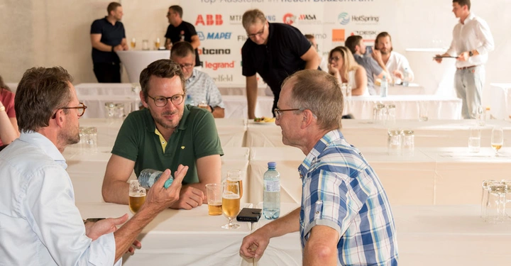 Galerie-Bild 2: Personen führen Gespräche an einem Tisch mit Getränken in einem hellen Raum; im Hintergrund unterhalten sich weitere Personen neben einem Tisch mit Sponsorlogos von ABB Mapei Litex Bticino und anderen.