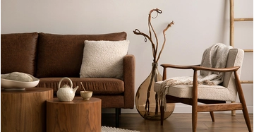Ein braunes Sofa mit texturiertem Kissen, Hölzmöbeln und einer auffälligen strukturellen Vase in stilvollen Erdtönen.
