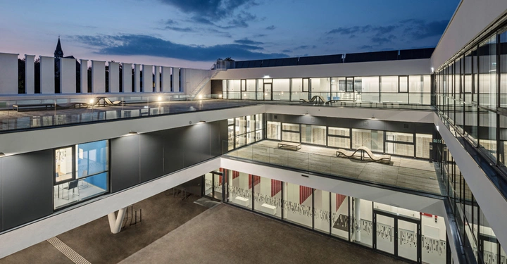 Galerie-Bild 13: Modernes Gebäude mit mehreren Stockwerken Blick von innen nach außen. Der Innenhof ist von Glaswänden und Balkonen umgeben. Im Hintergrund ist der Himmel bei Dämmerung sichtbar.