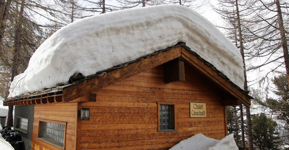 Holzhütte mit Schneedecke auf dem Dach stehend im verschneiten Wald mit Nadelbäumen umgeben Schild mit der Aufschrift Chalet Unschuld an der Wand befestigt