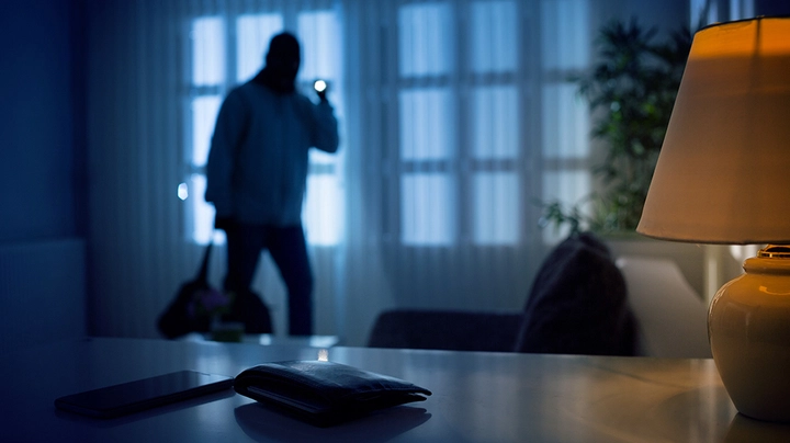 Ein Dieb bricht Nachts in ein ungesichertes Haus ein und leuchtet mit der Taschenlampe in die Dunkelheit.