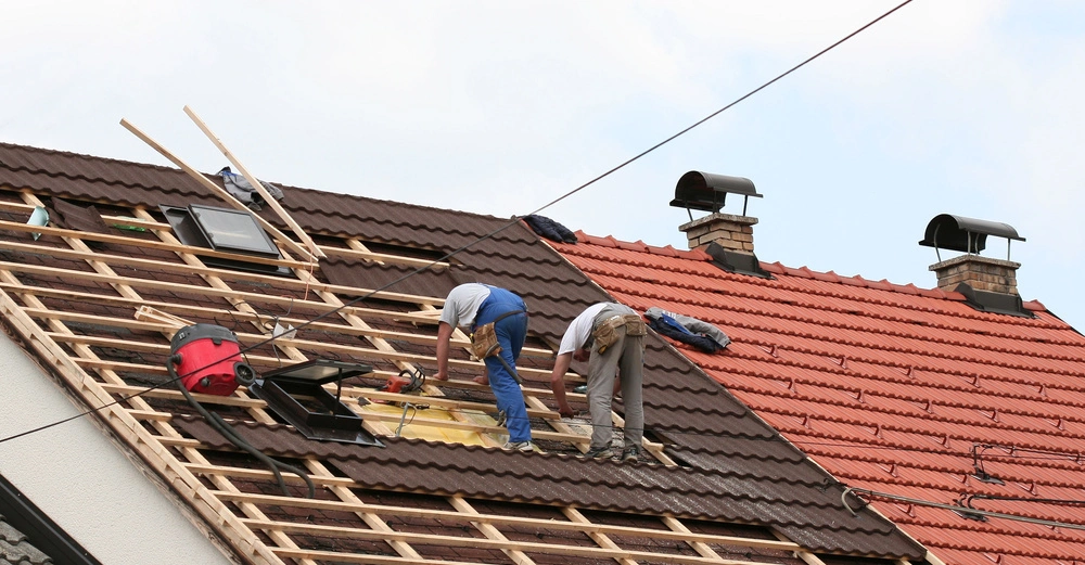 Zwei Handwerker arbeiten auf einem braunen Ziegeldach eines Hauses Kontexthintergrund sind Ziegel und zwei Schornsteine.