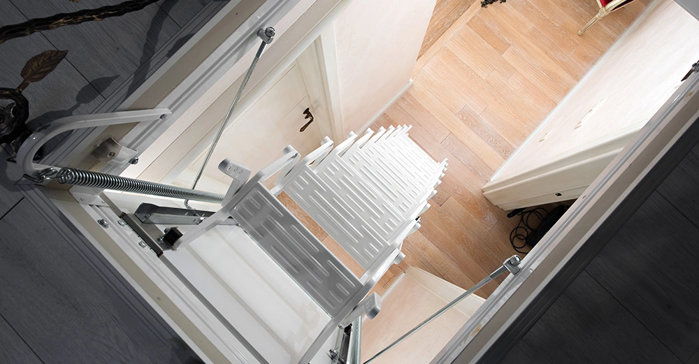 Leiter entfaltet sich in den Raum darunter mit Holzboden und einer geschlossenen Tür, Wände in hellem Ton, erkennbar ist ein Teil eines Stuhls und einer Lampe.