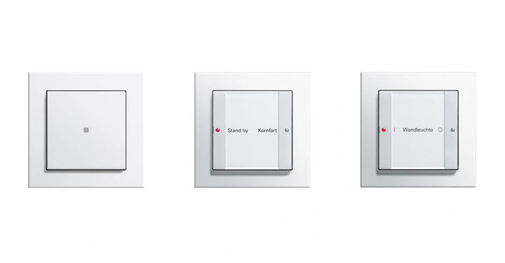 Drei Lichtschalter in einem weißen Rahmen. Der linke und mittlere Schalter besitzen jeweils eine kleine rote LED. Auf dem mittleren Schalter steht Stand by Komfort. Auf dem rechten Schalter steht Wandleuchte