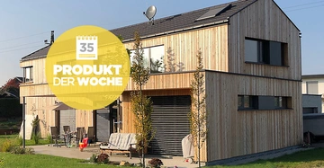 Zweistöckiges Holzhaus steht in einem Garten mit Möbeln und Spielzeug unter einem sonnigen Himmel. Gelbes Schild mit Text 35 PRODUKT DER WOCHE überlagert das Bild.