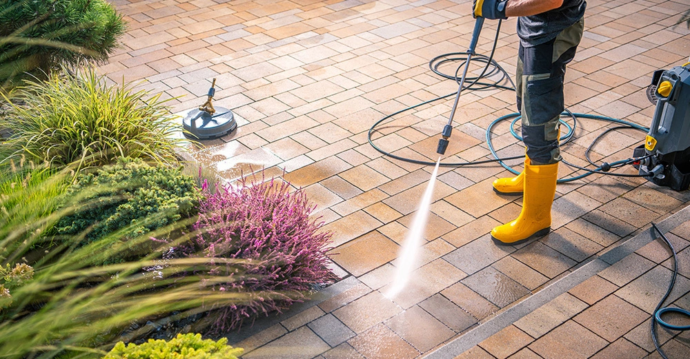 Terrassenreinigung mit Hochdruckreiniger im Garten. Saubere Pflastersteine und blühende Pflanzen an einem sonnigen Tag.