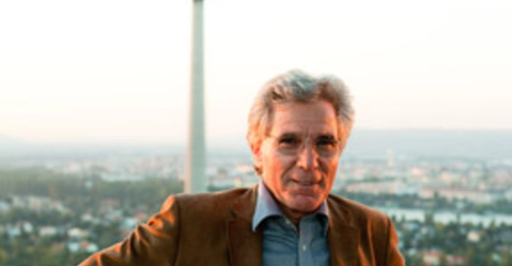 Galerie-Bild 21: Ein Mann steht lächelnd mit verschränkten Armen auf einem Balkon. Im Hintergrund befindet sich ein hoher Fernsehturm in einer grünen städtischen Landschaft.