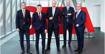 5 Männer in scharzen Anzügen stehen vor rotem STRABAG Logo