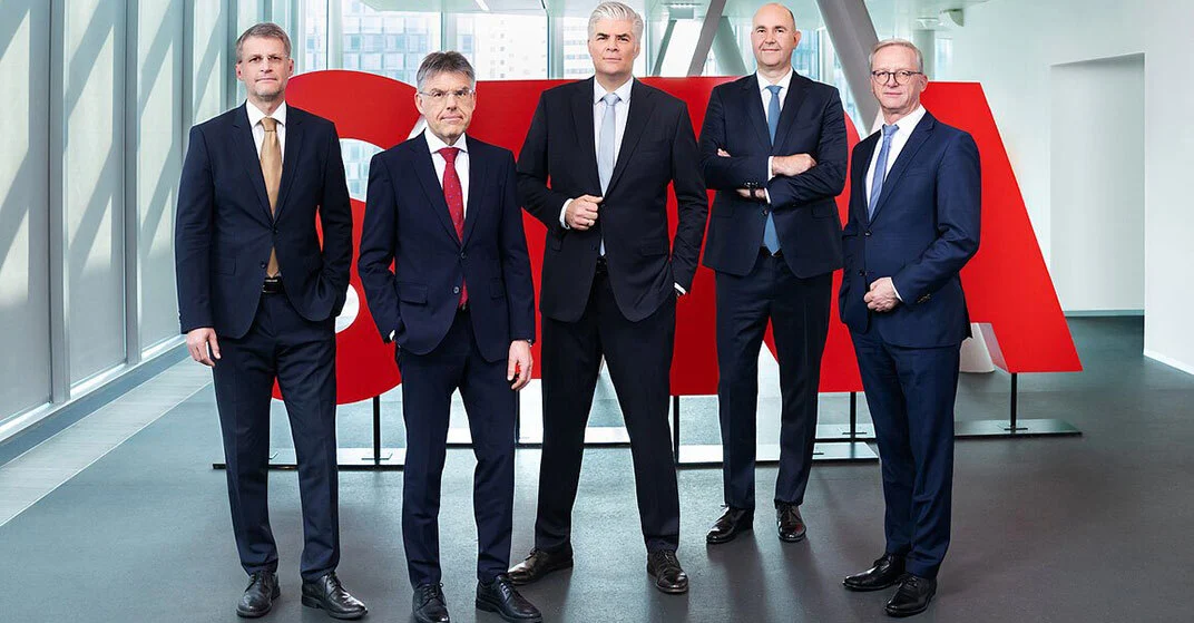 5 Männer in scharzen Anzügen stehen vor rotem STRABAG Logo