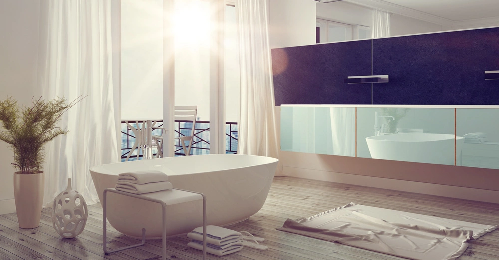 Freistehende Badewanne steht vor großen Fenstern im modernen Badezimmer mit Holzboden und weißen Vorhängen Sonnenlicht scheint herein Handtücher liegen auf einem Hocker und ein Teppich liegt daneben