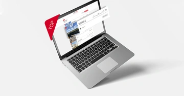 Ein Laptop zeigt eine Immobilien-Website mit Anzeigen für Häuser Preise beginnen bei 921.000 €. Ein roter Banner mit der Aufschrift TOP steht links. Der Laptop befindet sich auf einer weißen Oberfläche.