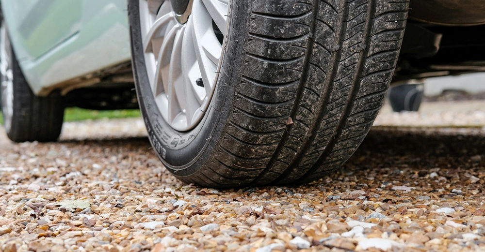 Großaufnahme eines Autoreifens, Auto fährt auf geschottertem Zugangsweg.