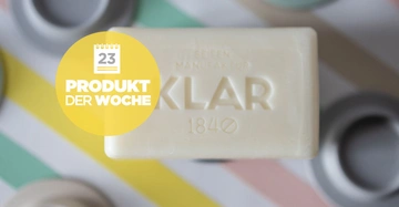 Eine weiße Seife mit der Aufschrift KLAR 1840 liegt auf einem gestreiften Hintergrund. Ein gelber Kreis zeigt den Text 23 PRODUKT DER WOCHE."