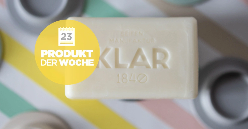 Eine weiße Seife mit der Aufschrift KLAR 1840 liegt auf einem gestreiften Hintergrund. Ein gelber Kreis zeigt den Text 23 PRODUKT DER WOCHE."