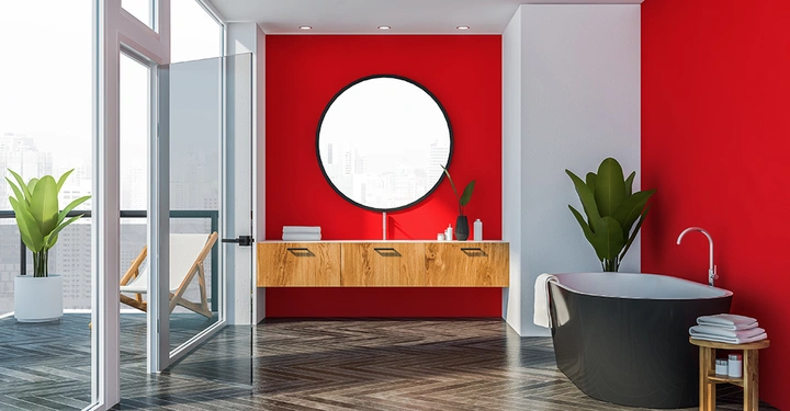 Moderne Badezimmerumgebung mit Holzmöbeln an einer roten Wand Hängendes Waschbecken mit Spiegel Pflanzen an beiden Seiten Freistehende Badewanne auf gemustertem Boden Offene Glastür führt zu Balkon mit Stadtblick