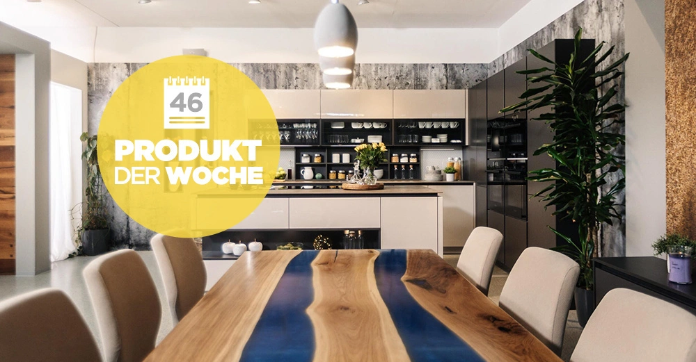 Holztisch mit blauer Epoxidharz-Mittelrille steht in einem modernen Esszimmer mit grauer Wand und Küchenschränken; große Pflanzen dekorieren den Raum. Text: 46 PRODUKT DER WOCHE.