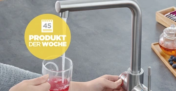 Hände bedienen einen modernen Wasserhahn, der in ein Glas mit rotem Getränk auf eine graue Küchenarbeitsplatte fließt. Auf dem Bild steht der Text: 45 PRODUKT DER WOCHE.