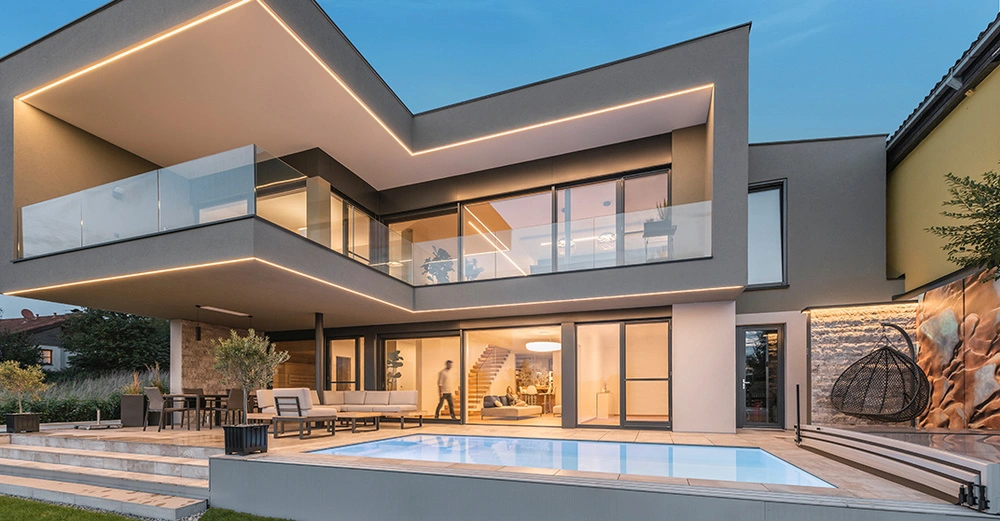 Modernes zweistöckiges Haus mit Glasbalustraden und LED-Beleuchtung Treppen innen offen Wohnzimmer Menschen interagieren Außenbereich mit Terrasse Möbeln und beleuchtetem Pool umgeben von Bäumen und dichtem Bewuchs