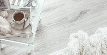 wunderschön weiß gekalkter Holzboden, darauf steht ein Tablett mit einer Tasse Tee und am Boden liegt eine weiße, grob gestrickte Wolldecke