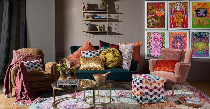 Mehrere bunte Kissen auf Sofas in einem stilvollen Wohnzimmer mit gemustertem Teppich Couchtischen mit Büchern und Vasen und farbenfrohen Gemälden an der Wand.