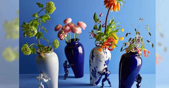 Galerie-Bild 5: Weiße und blaue Vasen mit bunten Blumenarrangements werden von kleinen Skulpturen menschlicher Figuren auf einem blauen Hintergrund gehalten