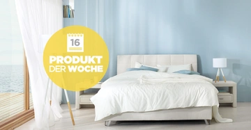 Bett steht im hellen Schlafzimmer mit blauen Wänden und weißen Vorhängen neben einem Fenster mit Meerblick Text auf gelbem Kreis 16 PRODUKT DER WOCHE