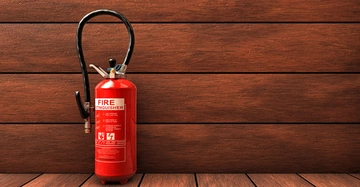 roter Handfeuerlöscher mit weißer Standardbeschriftung hängt vor vertäfelter Holzwand