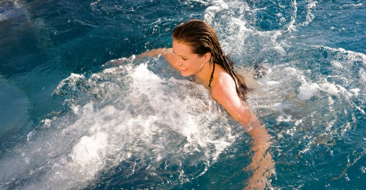 Frau schwimmt im sprudelnden Wasser eines Pools lächelnd.