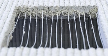 Ein rechteckiges Loch durchbricht eine graue, geflochtene Oberfläche. Fäden hängen lose im Loch und der Hintergrund ist dunkel.